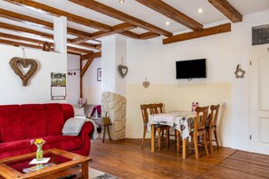 A living room with a red sofa, wooden dining table, and chairs, a stone wall, and a TV mounted on the wall.