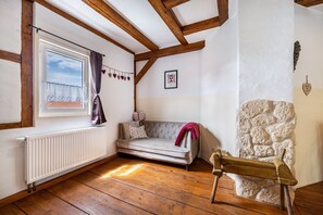 A room with a wooden floor, a white radiator, a sofa, a stone wall, and a window with curtains.