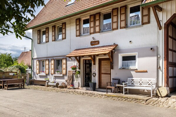 A two-story building with a sign reading 'Gasthof,' a wooden bench outside, and a white bench inside.