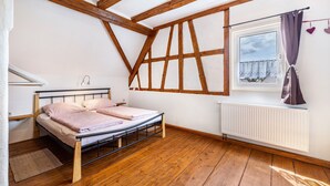 Un dormitorio con suelo de madera, una cama con cabecero, una ventana con cortinas y un radiador.