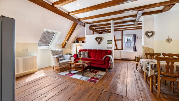 Una habitación tipo loft acogedora con un sofá rojo, suelo de madera y vigas de madera a la vista.