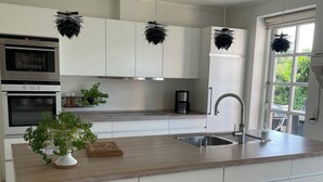 Una cucina moderna con mobili bianchi, un piano di lavoro in legno, forno integrato, macchina del caffè e una pianta in vaso.