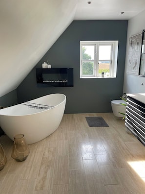 A modern bathroom with a freestanding bathtub, a window with a view, and a tiled floor.