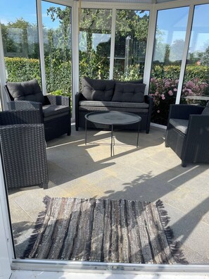 A covered outdoor seating area with wicker furniture, a cushioned sofa, and a round table. - Luxury country house in nature with wellness (Haderslev)