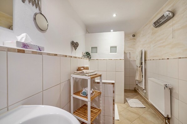 A bathroom with a white bathtub, a shelf with toiletries, a towel rack, and a radiator.
