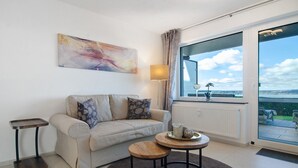 A modern living room with a sofa, a small round table, a floor lamp, and a large window with a view.