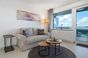 Ein modernes Wohnzimmer mit einer Couch, einem kleinen runden Tisch, einer Stehlampe und einem großen Fenster mit Blick.