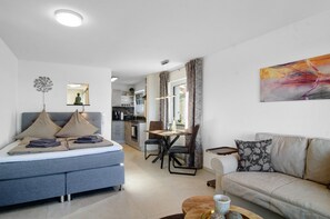Ein modernes Wohnzimmer mit Sofa, einem Esstisch und einer Küche im Hintergrund.