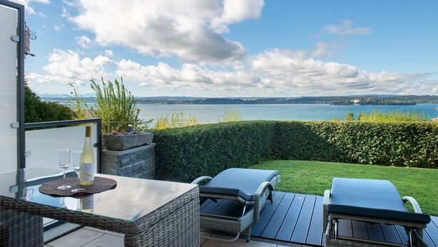 A patio with a glass table, two lounge chairs, and a bottle of wine.