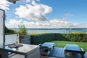 Une terrasse avec une table en verre, deux fauteuils et une bouteille de vin.