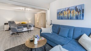 Ein modernes Wohnzimmer mit Sofa, Couchtisch, Schaukelstuhl, Bett und einem Gemälde an der Wand.