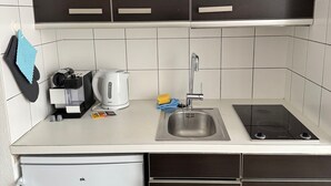 Eine Küche mit dunklen Schränken, einer weißen Arbeitsplatte, einem Spülbecken, einem Herd und einem kleinen Kühlschrank.