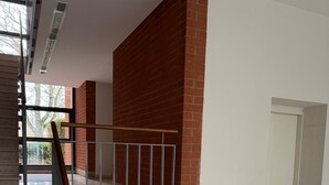 Ein großzügiger Innenraum mit Treppe, einer roten Backsteinwand und Blick durch große Fenster.