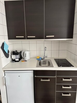 Una cocina con armarios oscuros, encimera blanca, fregadero, estufa y un refrigerador pequeño.