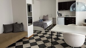 Una habitación compacta y moderna con cama, un escritorio pequeño, una silla y una kitchenette.