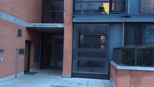 Un edificio con fachada de vidrio, una entrada visible y un pequeño espacio al aire libre con una banca.