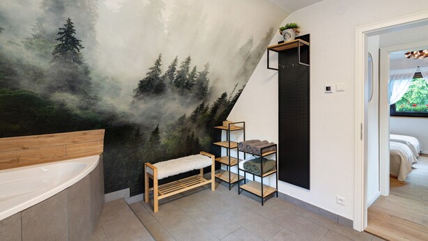 Une salle de bain ornée d’une grande fresque représentant une forêt, avec un banc en bois et une étagère où sont posées des serviettes.