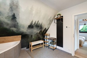 Un baño con un gran mural de bosque, un banco de madera y un estante con toallas.
