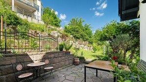 Une terrasse extérieure avec un sol en pierre, des chaises en métal, une table en bois et des plantes en pot.