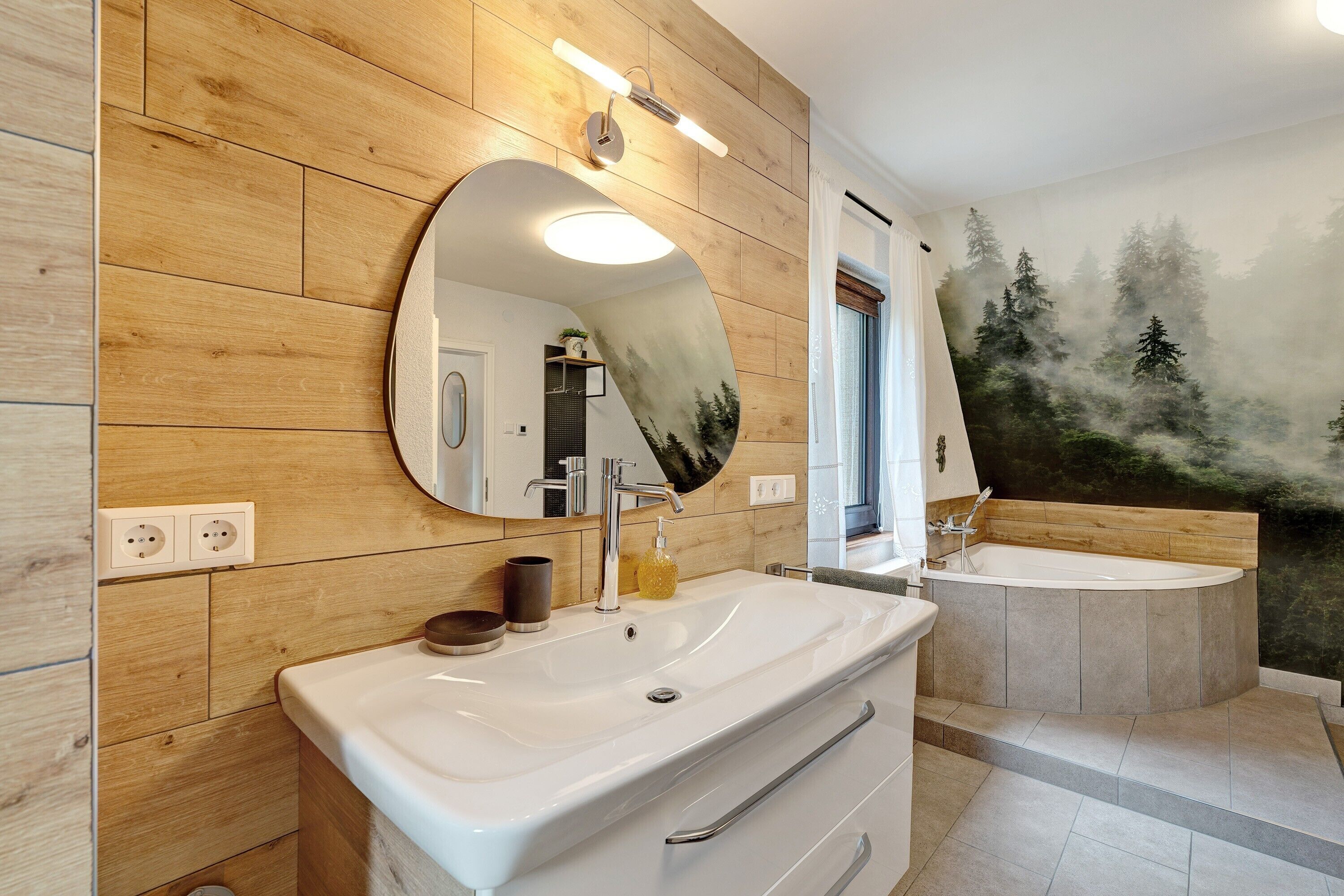 Une salle de bain avec un mur en bois, un grand miroir, un lavabo, une baignoire et une fresque représentant une forêt.
