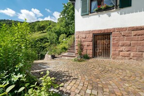 Un sendero de piedra que conduce a un edificio con puerta de madera, rodeado de vegetación y una ladera.