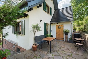 Un edificio blanco con contraventanas verdes, una puerta de madera y un patio de piedra con una mesa y sillas.