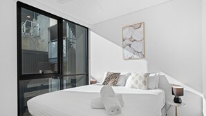 A modern hotel room with a large bed, a glass wall, a framed artwork, and a small table with a lamp. - Art House 2 King +Sofa Bed Free Parking Southbank (South Brisbane)
