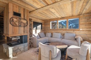 A cozy interior with a stone fireplace, a sectional sofa, and a large window offering a view of the outdoors. - Chalet Trevose⭐ Luxury • Hot Tub • Sauna • Close to the Slopes (Gerardmer)