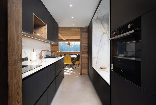 A modern kitchen with dark cabinetry, a marble countertop, and a built-in oven.