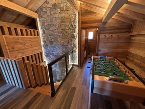 A room with a foosball table, wooden flooring, stone wall, and a glass railing.