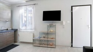 Een moderne keuken met een ingebouwde oven, een raam met gordijnen, een flatscreen televisie aan de muur en een deur met een handgreep.