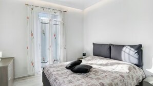 Een slaapkamer met een bed, nachtkastje, dressoir en een raam met gordijnen.