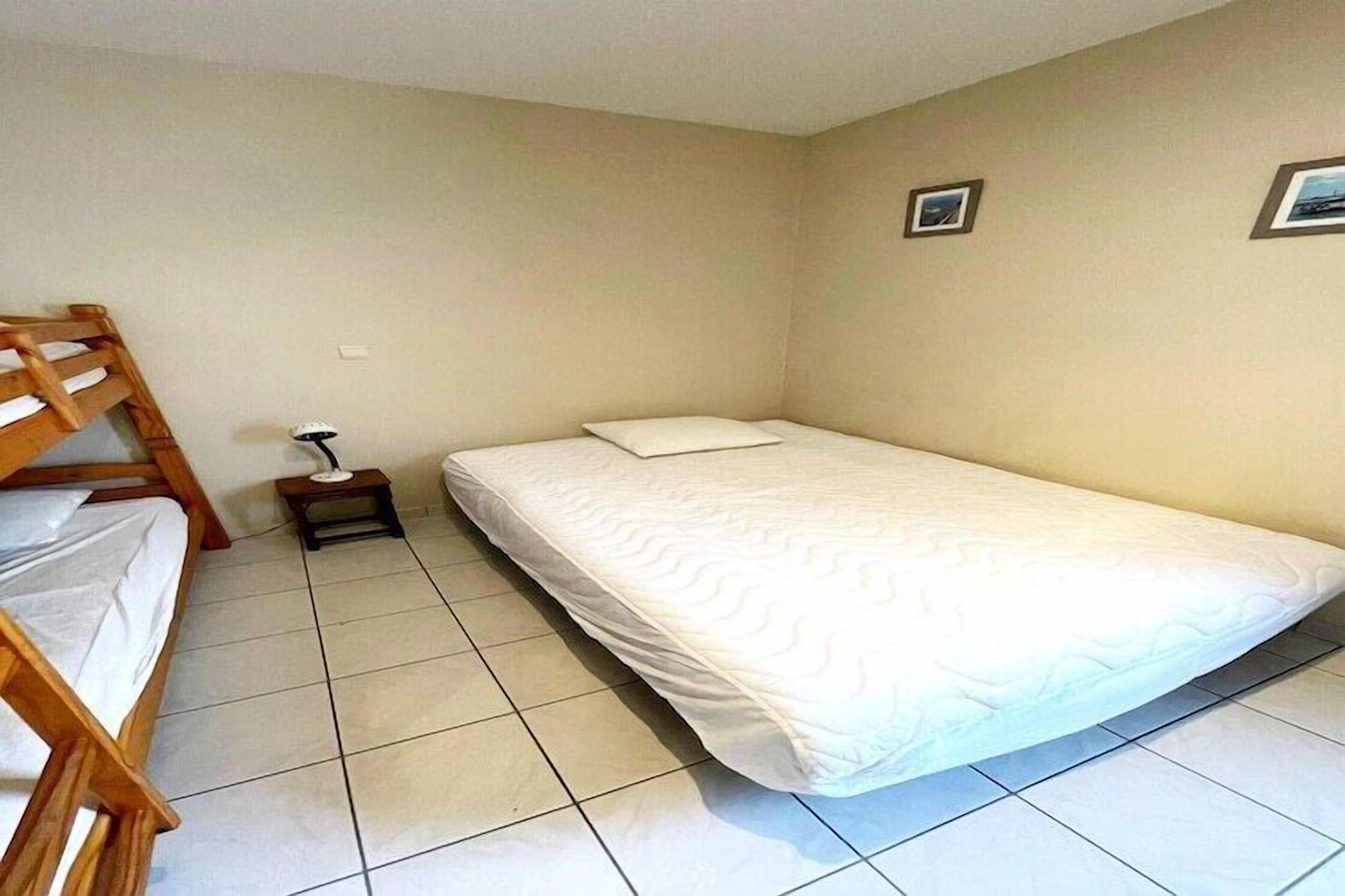 A small, clean room with a single bed, a wooden bunk bed, and a small table with a lamp.