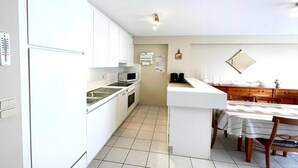 A compact kitchen with white cabinets, a microwave, and a sink. There is a dining area with a table and chairs. - Apartment by Belgian Coast with Sea View (MIDDELKERKE)