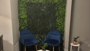 A small room with two blue chairs, a round table, and a green wall with a vertical garden. - Cozy Retreat w/ LED & Balcony (Charlotte)