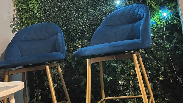 Two blue chairs with wooden legs and a small white table, positioned in front of a wall covered with green foliage and blue decorative lights. - Cozy Retreat w/ LED & Balcony (Charlotte)