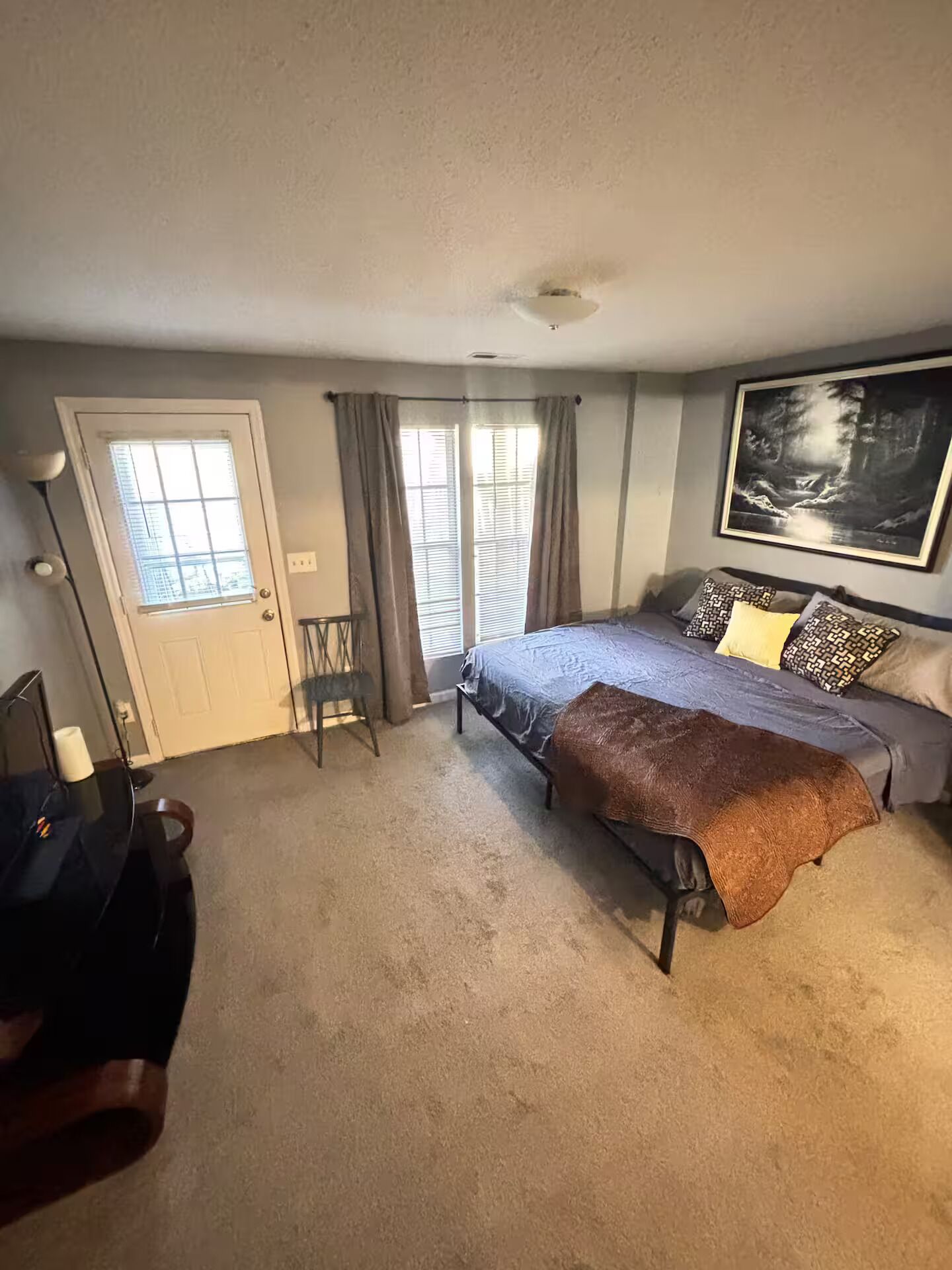 A bedroom with a bed, a desk, a chair, a window with curtains, and a painting on the wall.