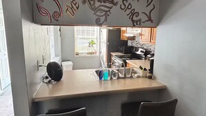 A compact kitchen with a countertop and two chairs, a small sink, and a decorative sign above the counter. - Cozy Retreat w/ LED & Balcony (Charlotte)