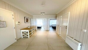 A hallway with a white door on the left, a white radiator on the right, and a small table with a lamp in the center.