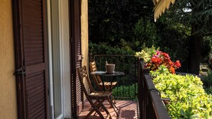 Un balcone con una sedia e un tavolo di legno, immerso nel verde e ricco di piante.