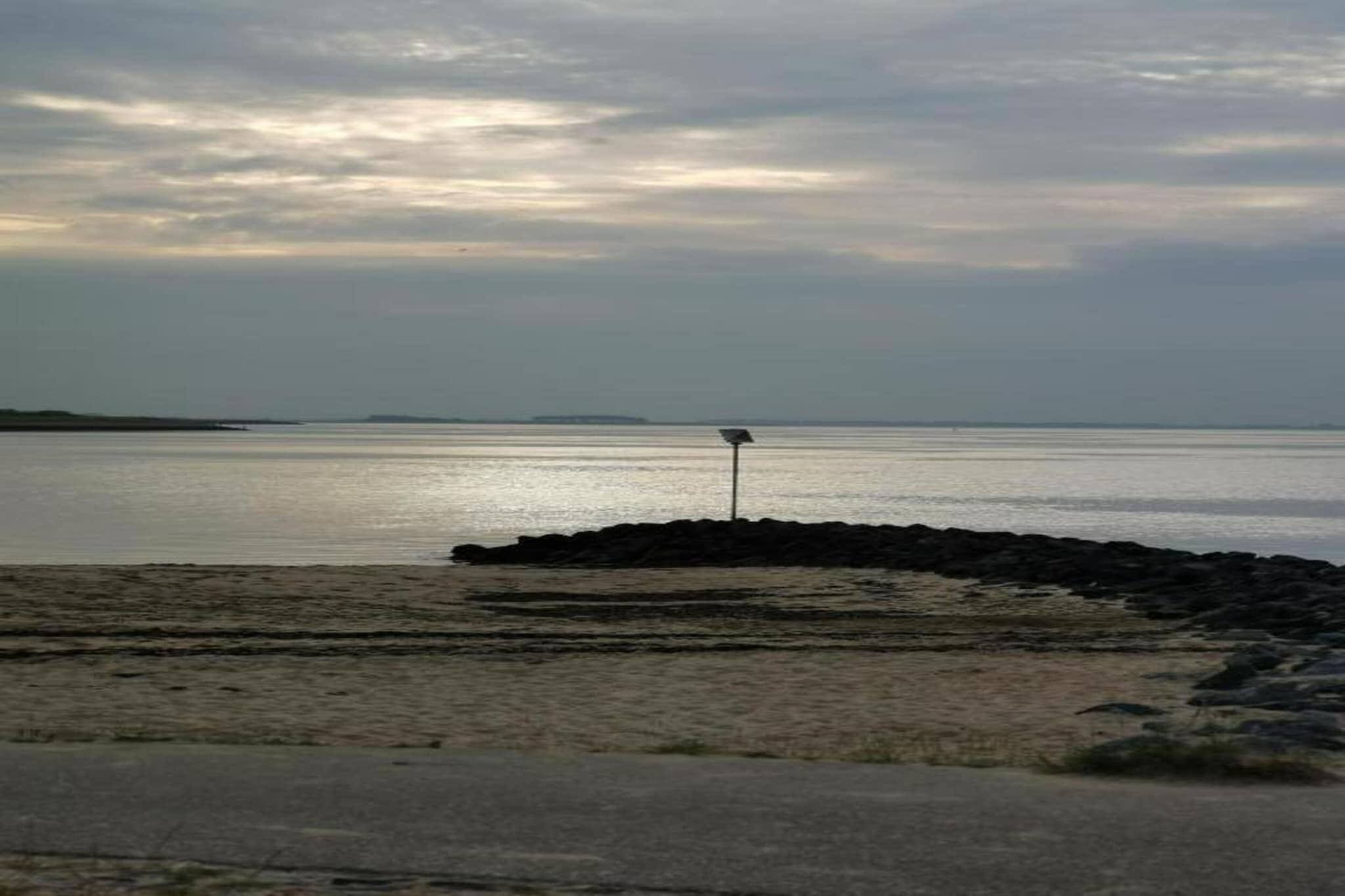 A beach with a rocky outcrop and a signpost in the distance.