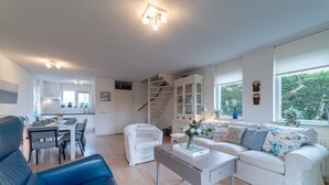 En moderne stue med en hvid sofa, en blå lænestol og et spiseområde med et bord dækket til seks personer.