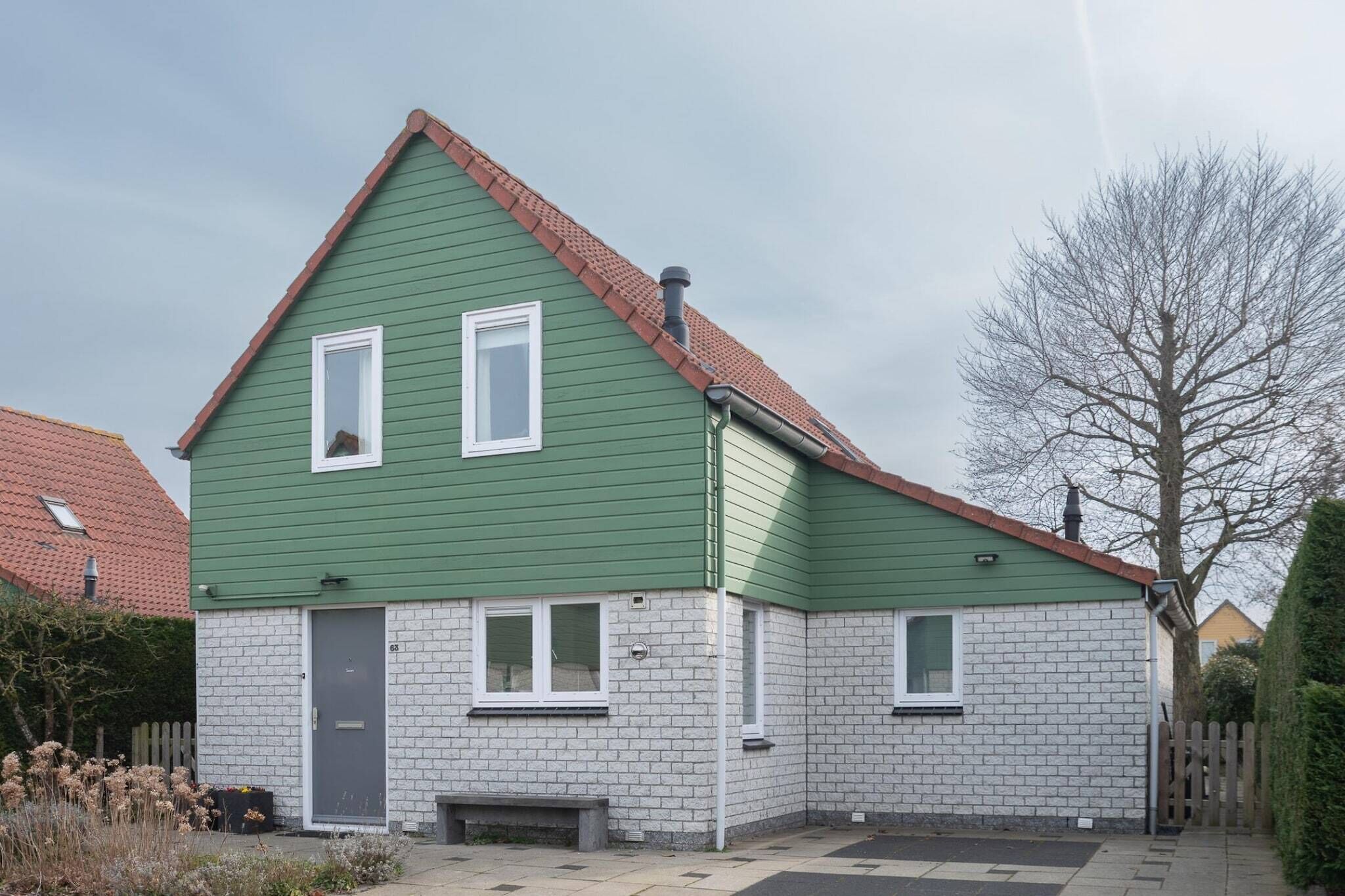 Une maison à deux étages, avec une façade verte et une base en briques blanches.