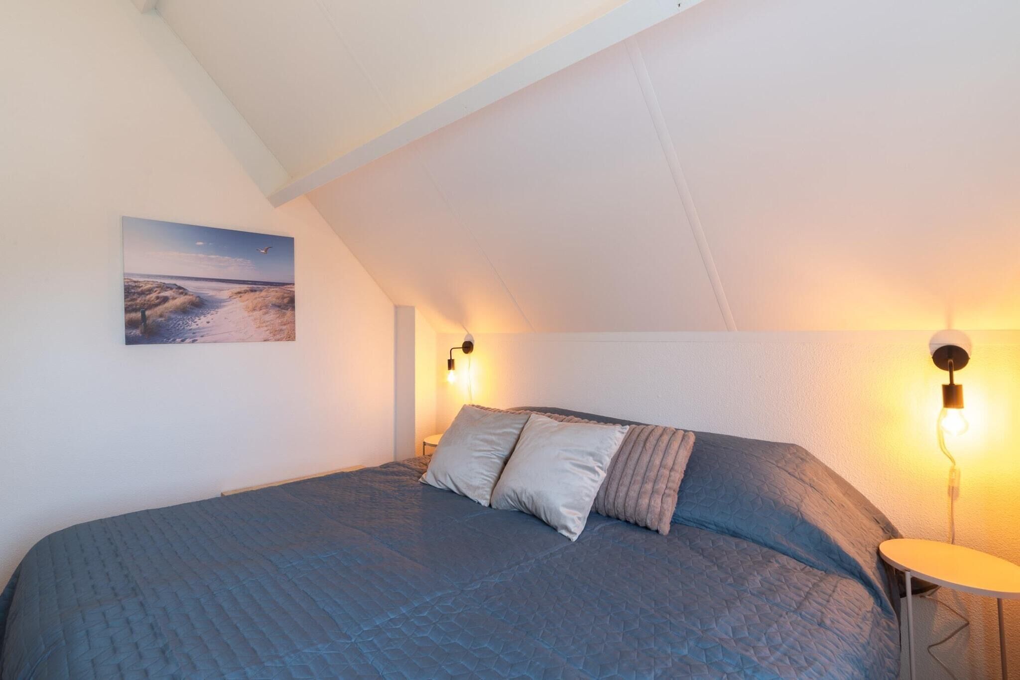 A bedroom with a large bed, two wall-mounted lamps, and a painting of a beach scene.