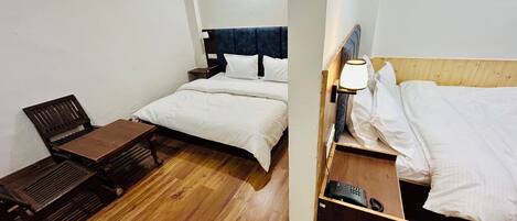 A small, compact hotel room with a single bed, a wooden nightstand with a lamp, a small table, and a chair.