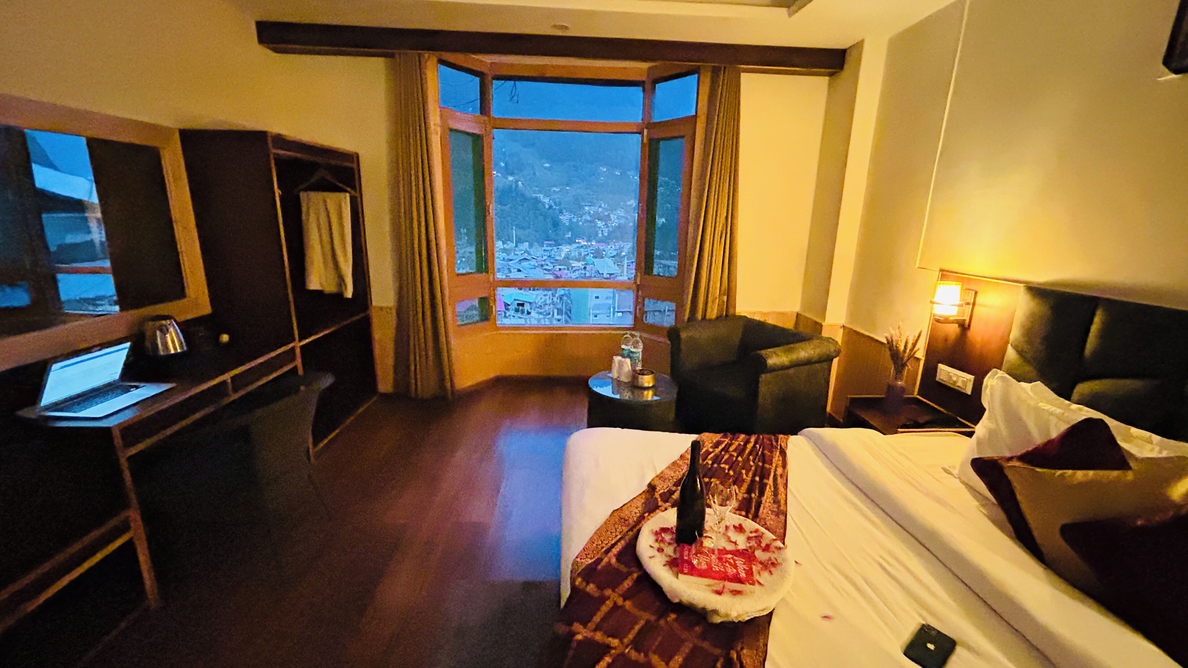 Une chambre d’hôtel avec un lit, un bureau avec un ordinateur portable, une chaise, une table de chevet avec une lampe et une fenêtre donnant sur la ville.