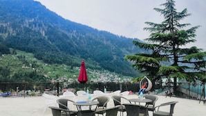 Une terrasse dotée de meubles en osier, d’un parasol rouge et offrant une vue sur un paysage montagneux.