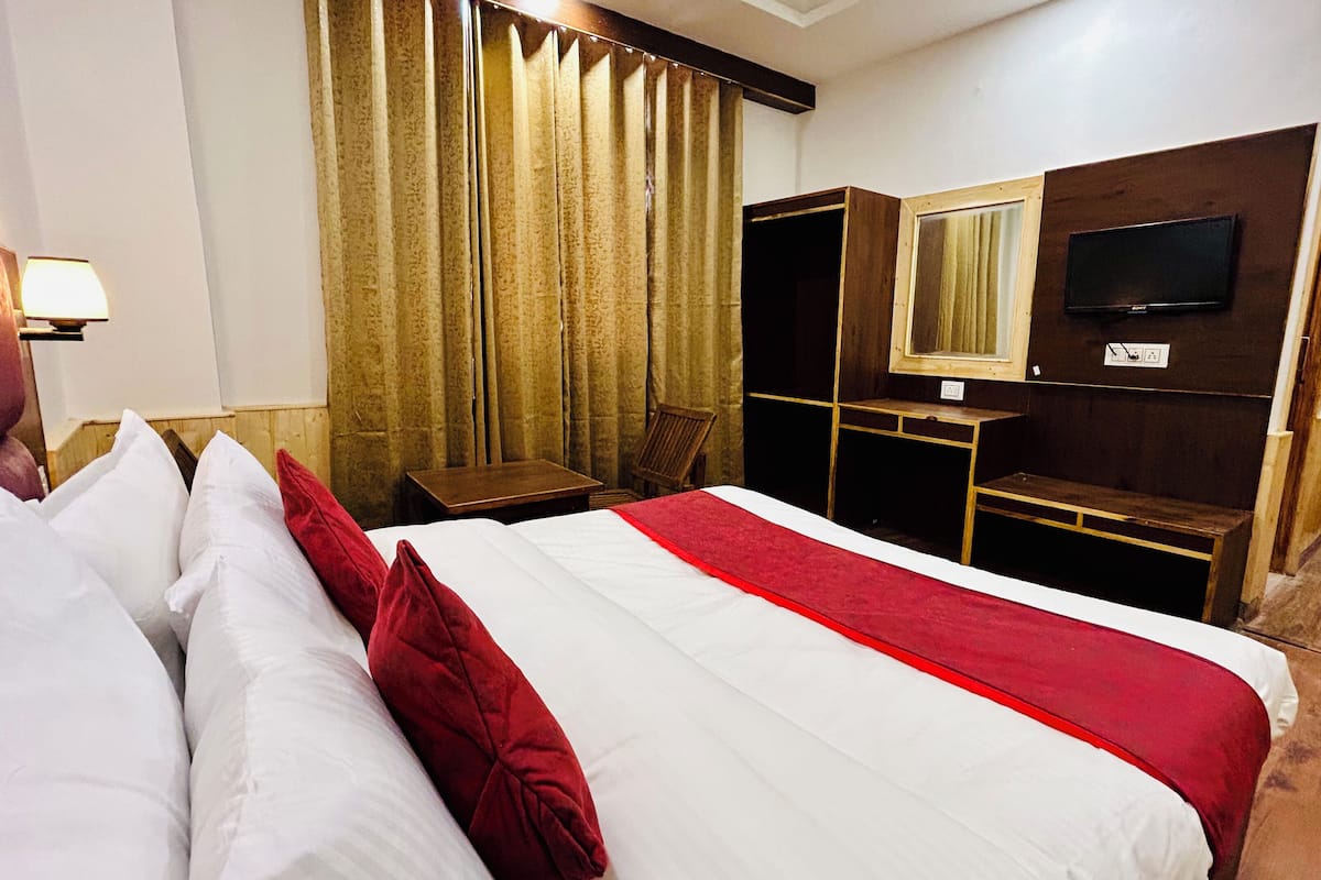 A hotel room with a large bed, a desk, a chair, a television, and a wardrobe.