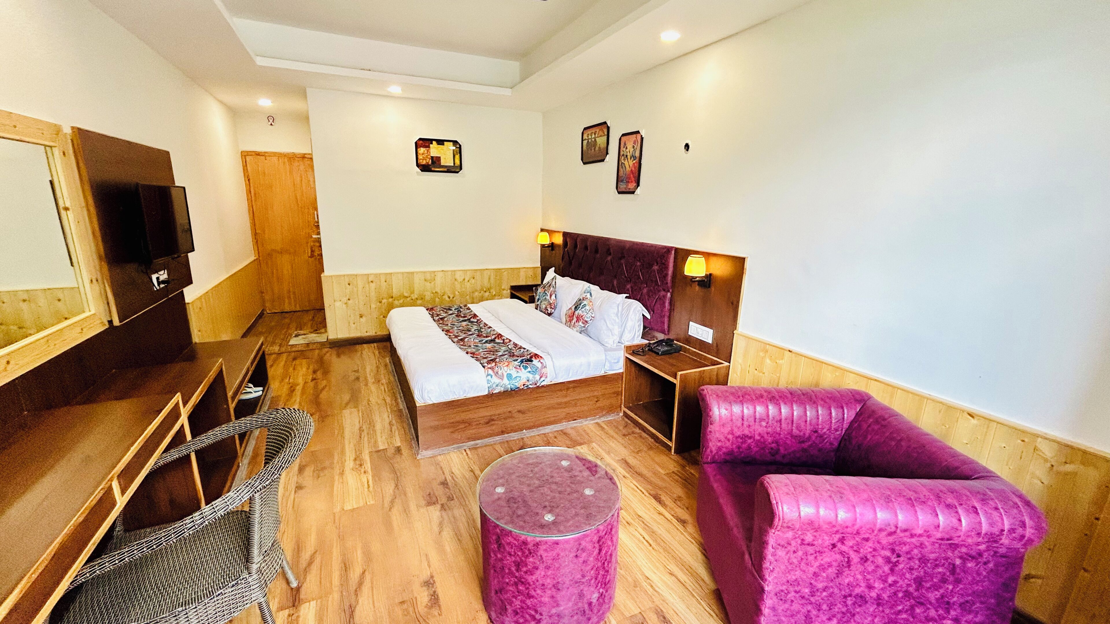 A hotel room with a bed, a wooden desk, a chair, a small round table, and a pink sofa.