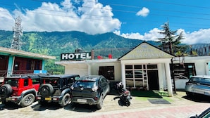 Un hôtel appelé « Hotel Ocean Manali », avec une enseigne, des véhicules garés et un paysage montagneux en arrière-plan.
